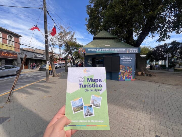 Mapa turístico de Quilpué en mano, frente a la Oficina de Información Turística en Plaza Irarrazabal, destacando atractivos culturales y naturales.