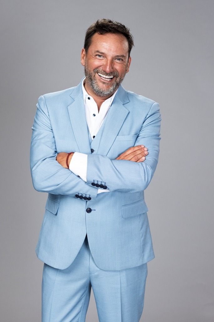 Daniel Fuenzalida, conductor de "Ahora Caigo" (TVN), sonríe con traje celeste. Lidera sintonía.