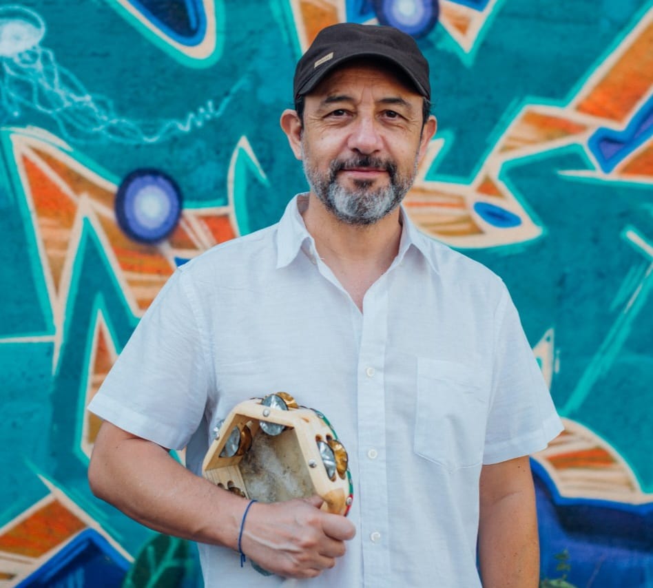 Daniel Muñoz, director de "Cantando a la Vida" y Taller A Viva Voz, con pandero y gorra. Mural vibrante.