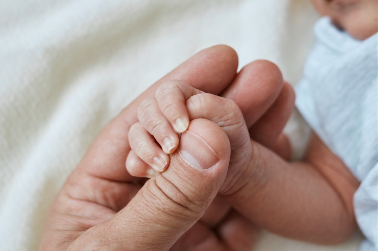 Mano de bebé sujetando dedo adulto. 11 guaguas con "síndrome del hombre lobo" por minoxidil accidental.
