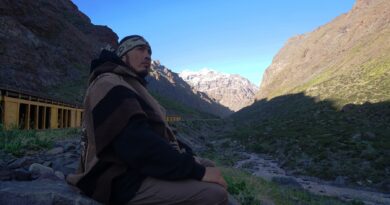 Neculman, rapero mapuche, con poncho andino en la Cordillera de Los Andes. Medita ante montañas nevadas. Videoclip 'Andes'.