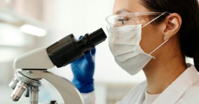 Investigadora en laboratorio, con mascarilla y gafas, usa microscopio. Representa el futuro de la mujer en STEM.