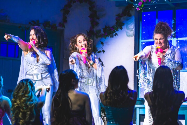 Mamma Mía! en Teatro Municipal Viña del Mar. Actrices con trajes brillantes y micrófonos rosas cantan en escena.