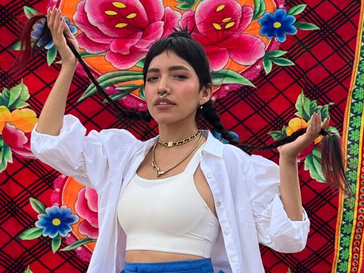 Renata Flores, Reina del Rap Quechua de Perú, con trenzas y joyas, frente a textil andino floral. Viña 2025.