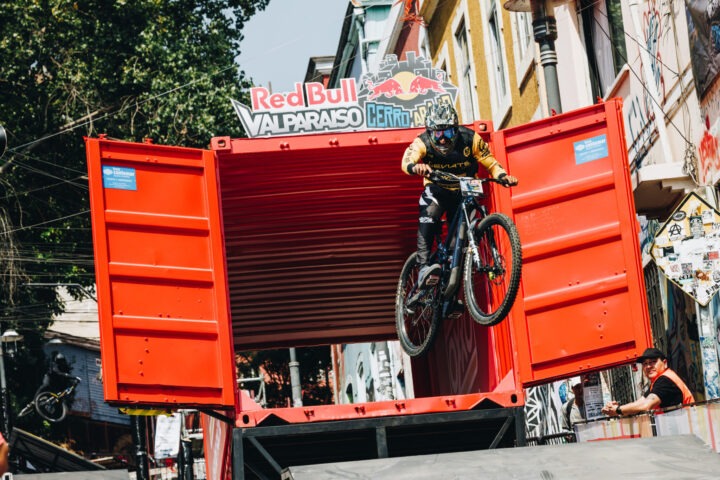 Ciclista de descenso urbano Red Bull Valparaíso Cerro Abajo saltando un contenedor rojo. Acción extrema en Valparaíso.