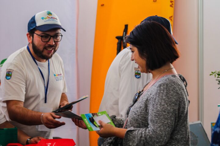 Hombre de Puchuncaví entrega folletos de destinos turísticos a una mujer en la Feria Internacional FITVAL Valparaíso Región.