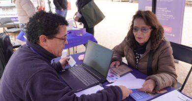 Funcionario IPS ChileAtiende asiste a adulta mayor con solicitud PGU en mesa con laptop y documentos.