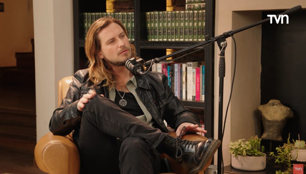 Jean Philippe Cretton, animador, en el podcast Mamá por Siempre de TVN. Sentado, con micrófono, estantería de libros.