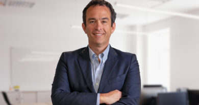 Hombre profesional sonriente con traje azul, brazos cruzados, fondo de oficina.