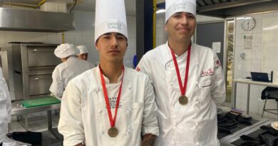 Dos chefs de Santo Tomás con gorros y medallas de bronce en cocina profesional. Reconocimiento gastronómico.