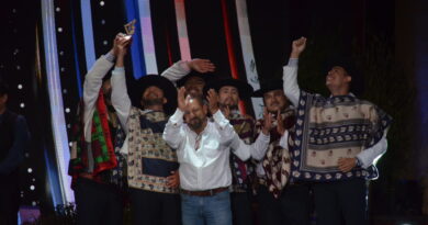 Grupo de artistas folclóricos celebrando en escenario, uno levanta un trofeo. Visten ponchos y sombreros. Premiados por su música.