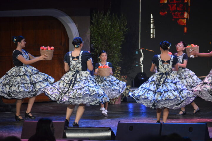Danza folclórica en Festival Olmué 2026. Bailarinas con vestidos típicos y canastas de fruta vibran en el escenario.