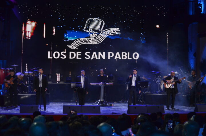 Los de San Pablo: cuarteto vocal de Limache en concierto. Escenario con banda, luces, pantalla LED con logo y público.