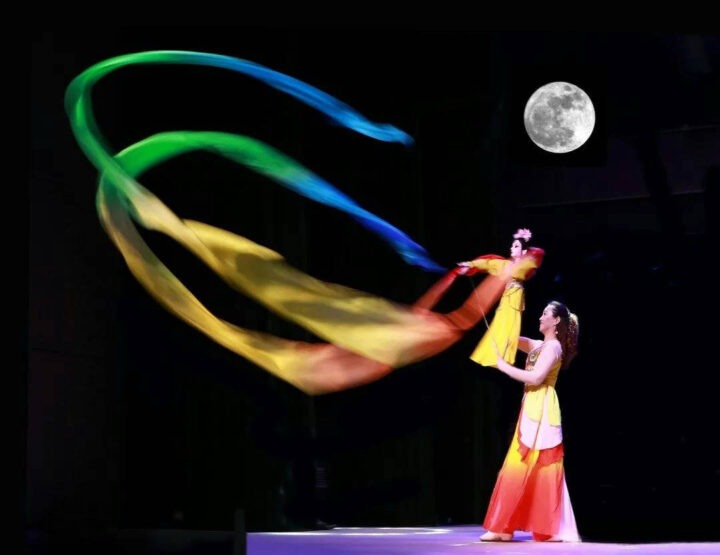 Danza china tradicional. Bailarina con títere y largas sedas coloridas en escena nocturna bajo la luna llena.