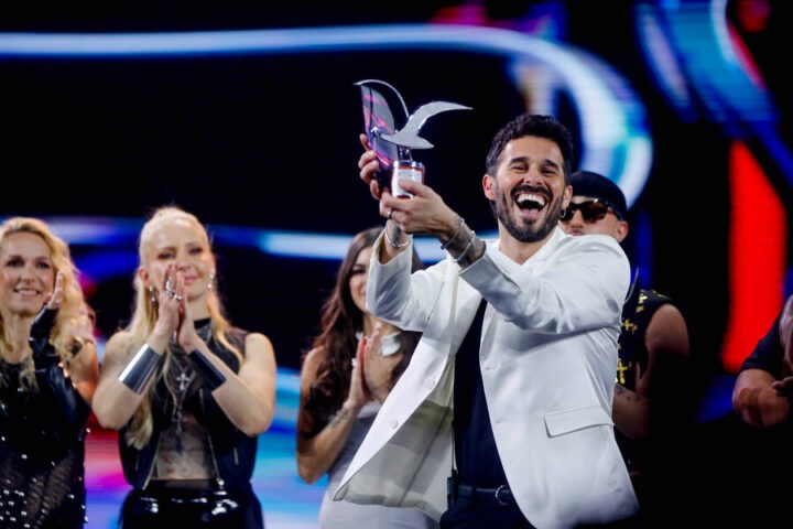 Ganador sonriente levanta Gaviota de Plata. Otros artistas aplauden en el festival.