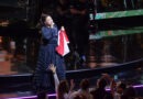 Gloria Estefan en el escenario de Viña del Mar, cantando con vestido negro, sosteniendo bandera chilena, público emocionado.