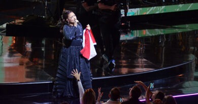 Gloria Estefan en el escenario de Viña del Mar, cantando con vestido negro, sosteniendo bandera chilena, público emocionado.