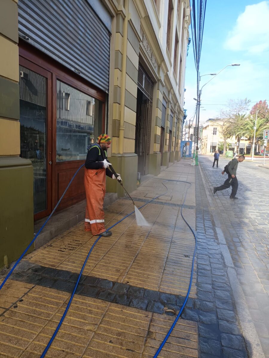 Trabajador municipal usando hidrolavadora en una calle de Valparaíso.