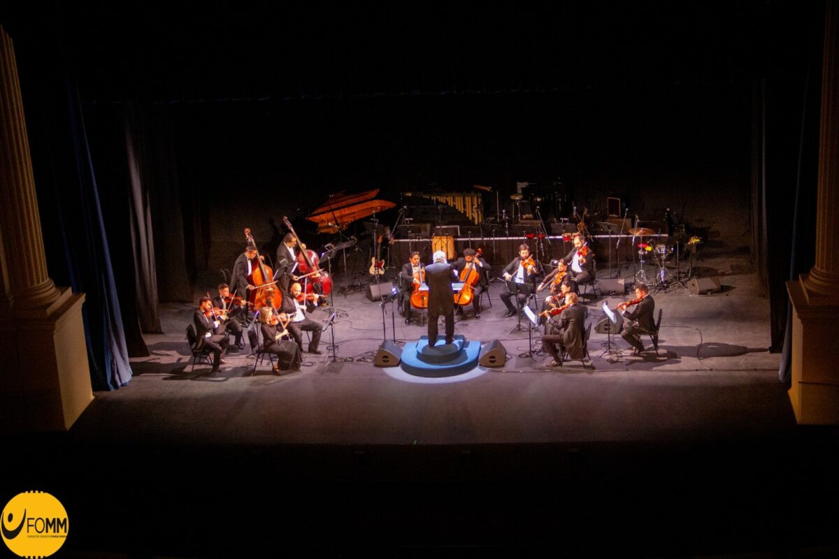 La Orquesta Marga Marga interpretando una pieza musical en un escenario oscuro.