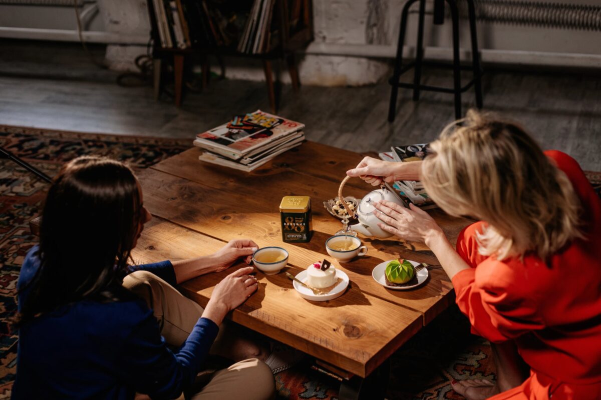 Dos personas compartiendo té y postres en una mesa de madera, simbolizando un momento de pausa y bienestar.