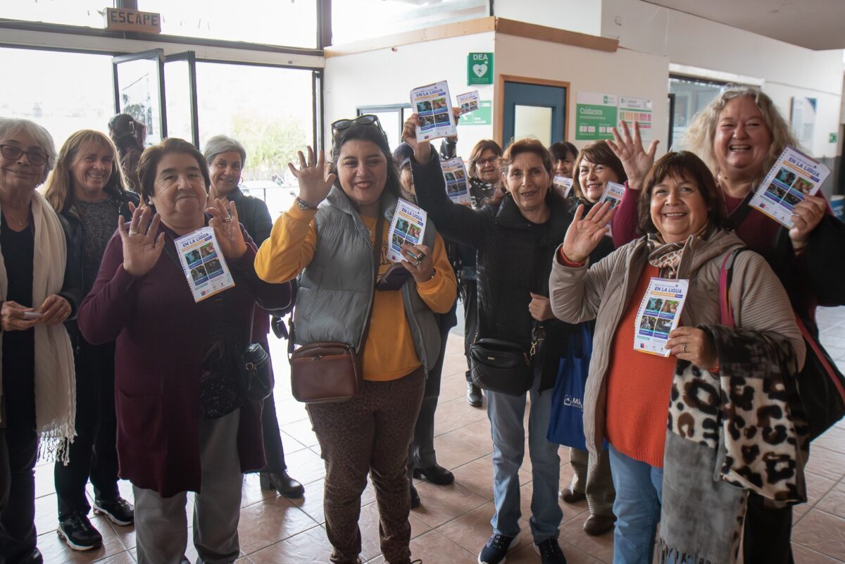 Un grupo de mujeres sonriendo y saludando, sosteniendo folletos.