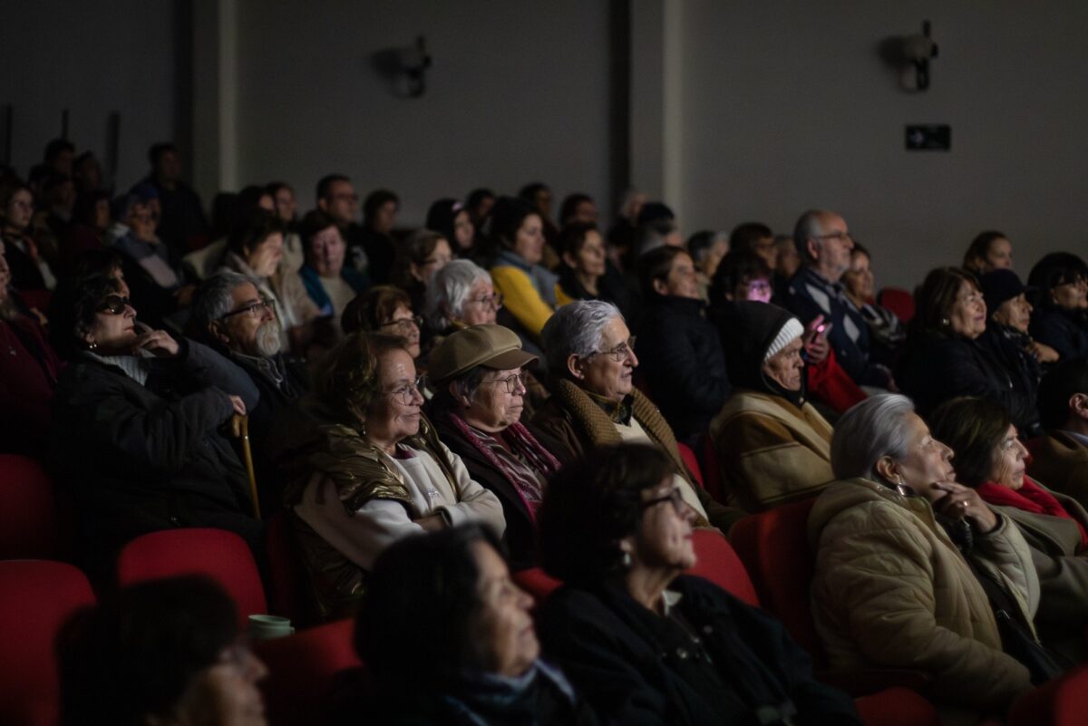 Público asistiendo a una función de cine, sentados en butacas rojas.