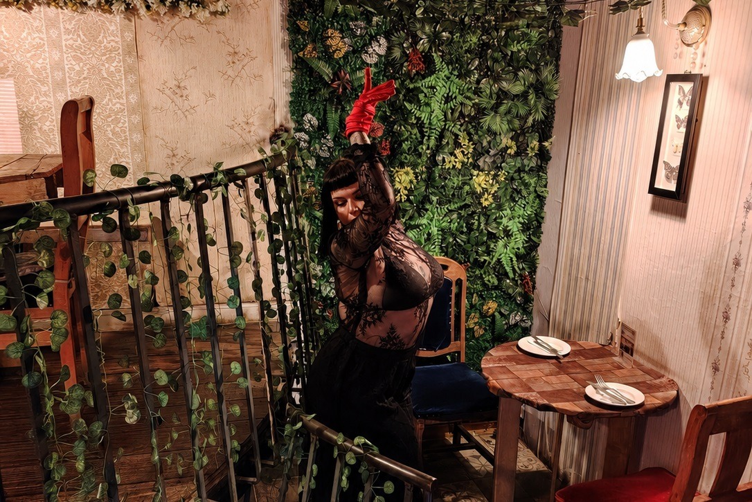 Olivia Mortis posando junto a una escalera de caracol en un ambiente íntimo.