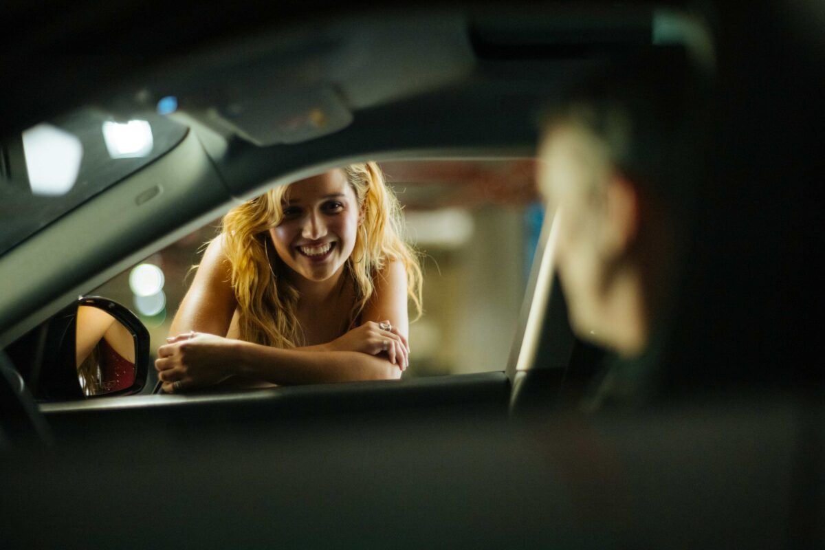 Una joven sonriente dentro de un automóvil mirando a alguien a través de la ventanilla.