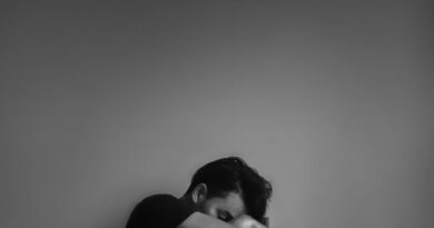 Hombre joven sentado encogido con la cabeza entre las rodillas, en blanco y negro.