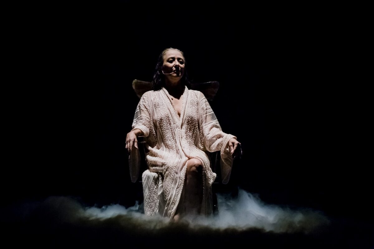 Intérprete sentada en escena bajo un foco de luz en la obra THITA.