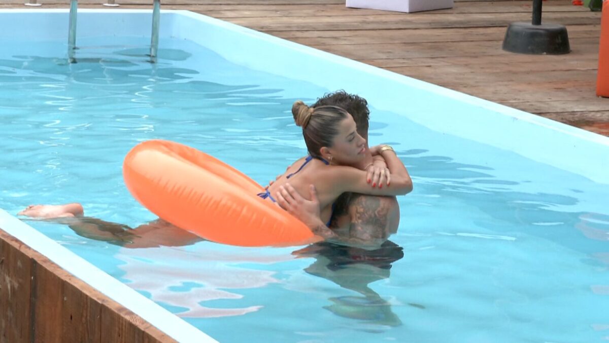 Pareja abrazándose mientras flota en una piscina con un inflable naranja.