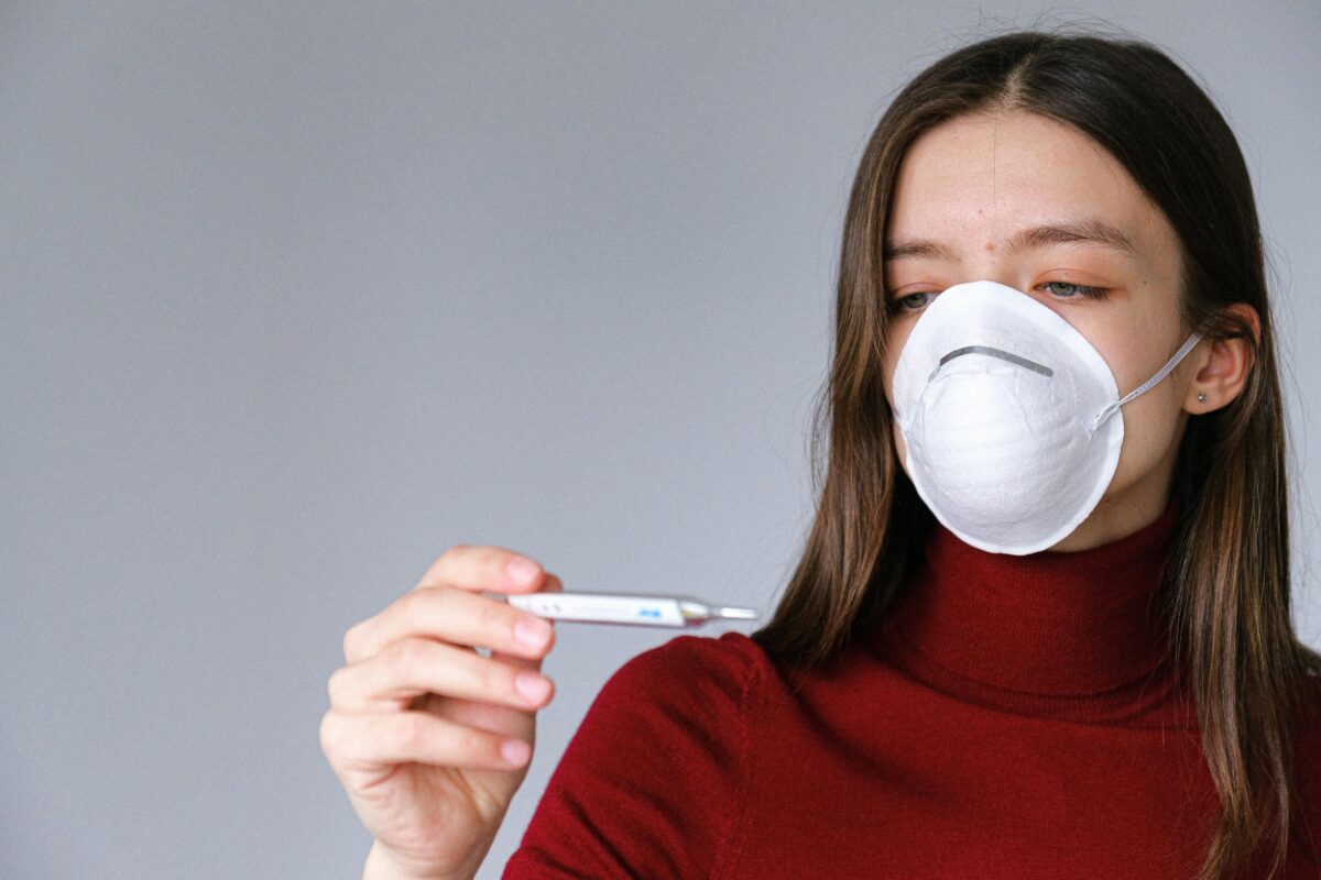 Mujer con mascarilla y termómetro, símbolo de prevención de enfermedades respiratorias.