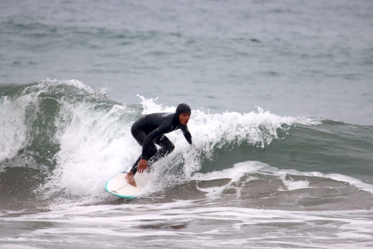 Joven surfista en traje de neopreno oscuro surfeando una ola en Playa El Bato.