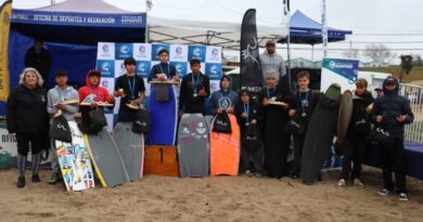 Grupo de jóvenes deportistas posando con sus trofeos y tablas en la arena de Playa El Bato, Quintero.