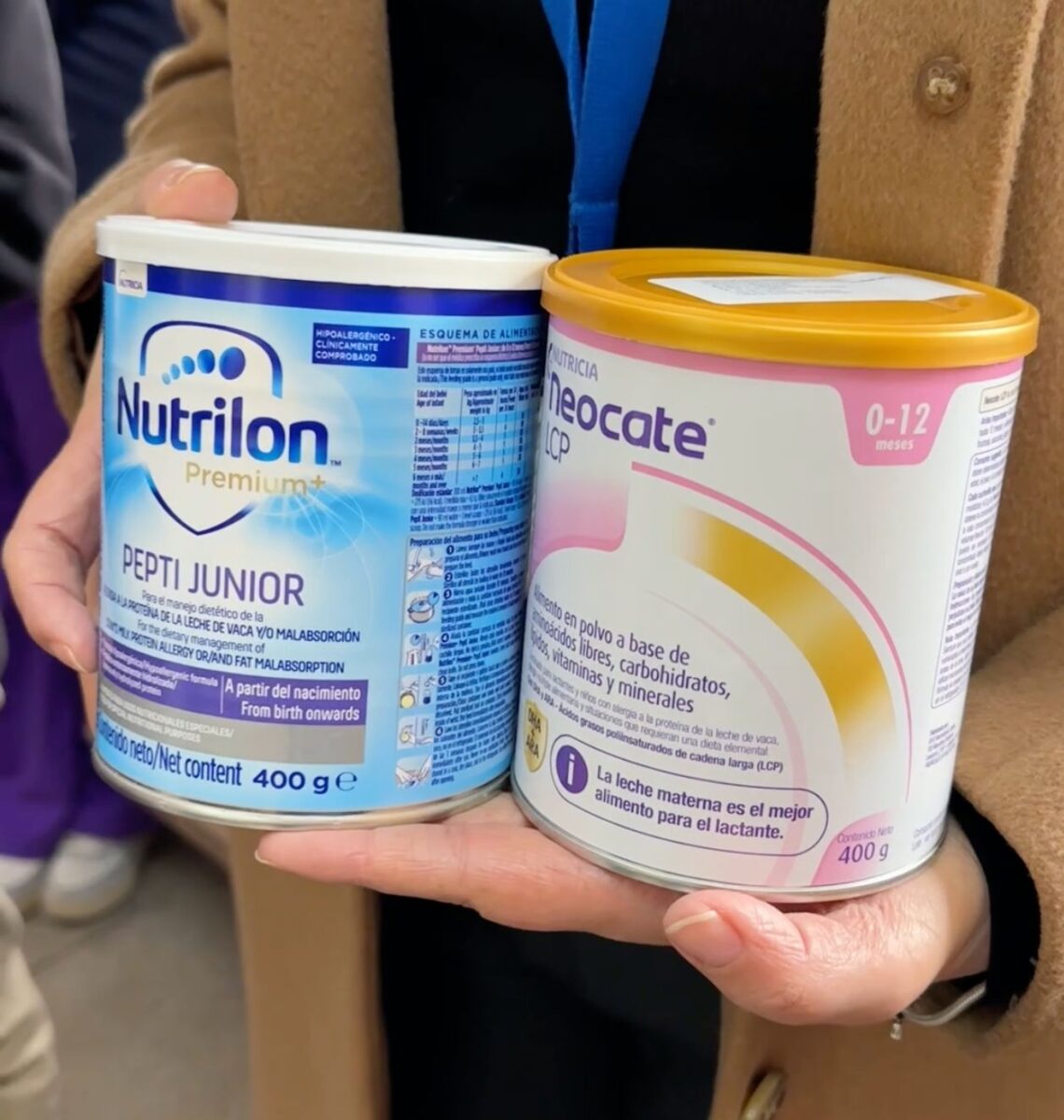 Manos sosteniendo latas de fórmulas lácteas Nutrilón y Neocate.