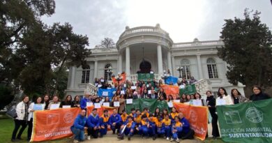 Grupo de personas, entre estudiantes y adultos, posando con banderas y certificados de educación ambiental frente a un edificio.