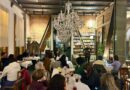 Interior del restaurant Da Mafalda, mostrando a comensales y un músico tocando la guitarra en un ambiente acogedor con un gran candelabro y estanterías de libros.