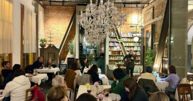 Interior del restaurant Da Mafalda, mostrando a comensales y un músico tocando la guitarra en un ambiente acogedor con un gran candelabro y estanterías de libros.