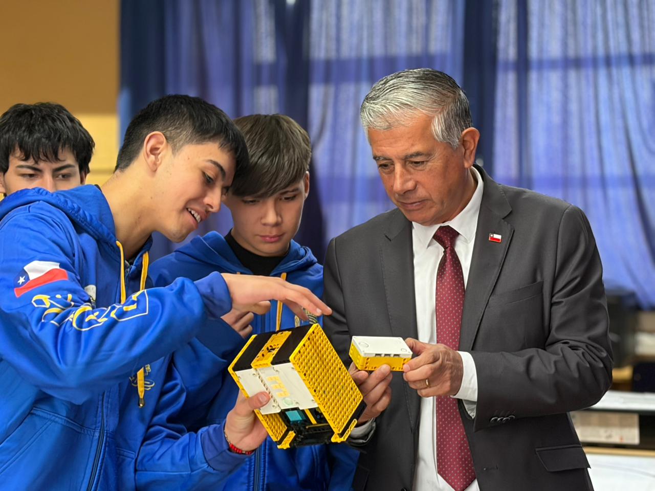 El Delegado Presidencial Regional de Valparaíso, Manuel Millones, observando un robot mientras dos estudiantes del taller R2D2 lo explican.