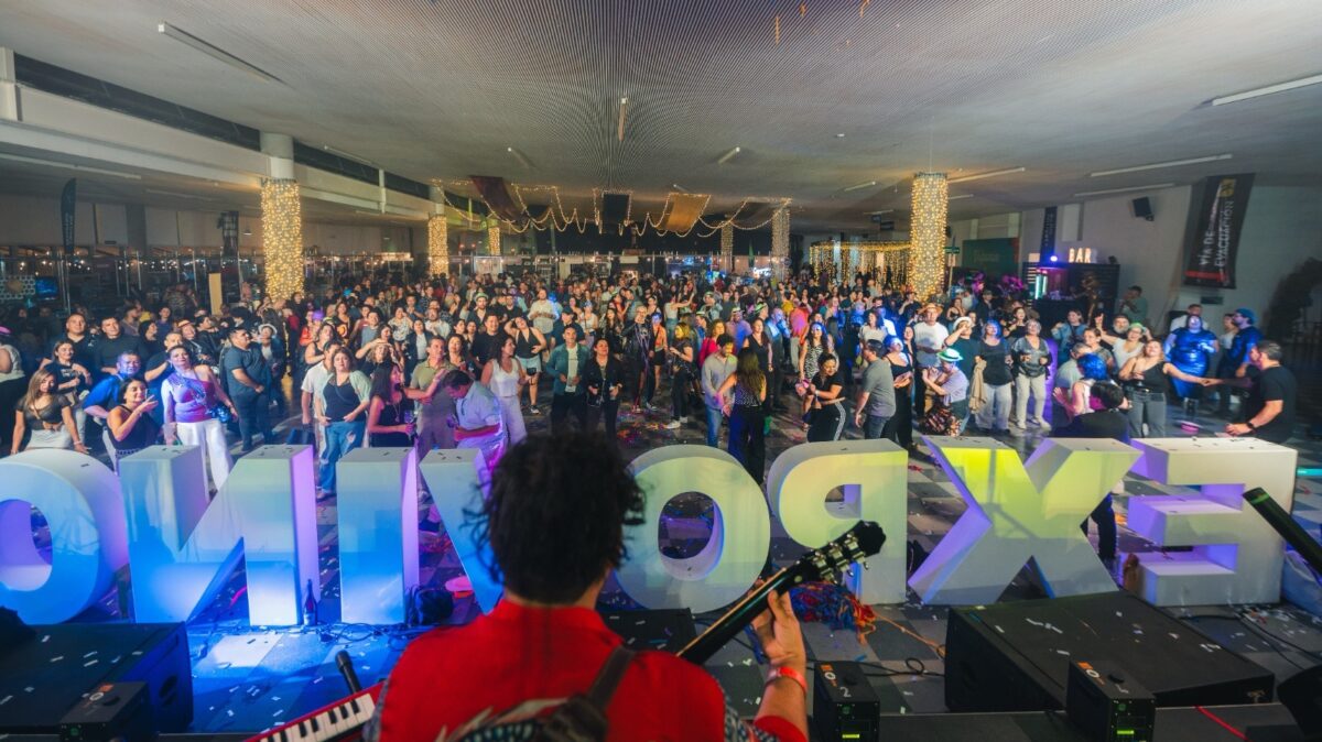Una multitud animada disfruta de un concierto con un escenario luminoso y letras grandes de 'EXPOVI'.