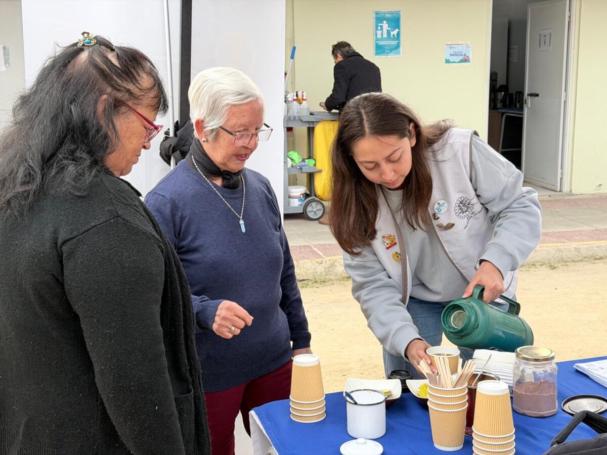 Una persona sirviendo té o café a dos adultos mayores en un puesto de la feria.
