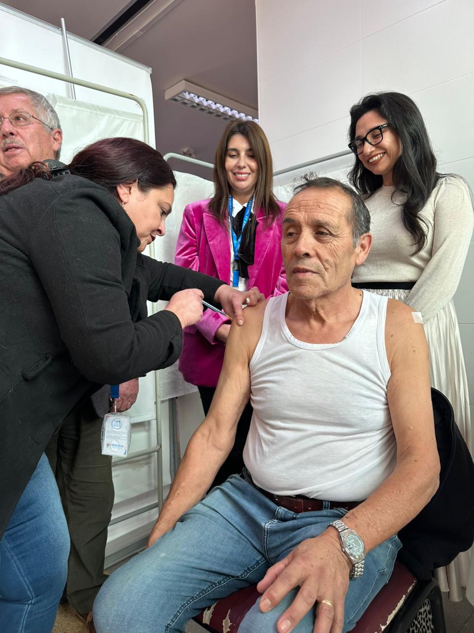 Hombre siendo vacunado por personal de salud, con autoridades observando la acción.