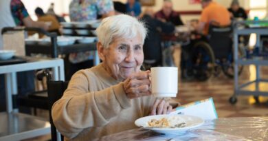 Adulto mayor sonriendo mientras sostiene una taza en el comedor de Fundación Las Rosas.