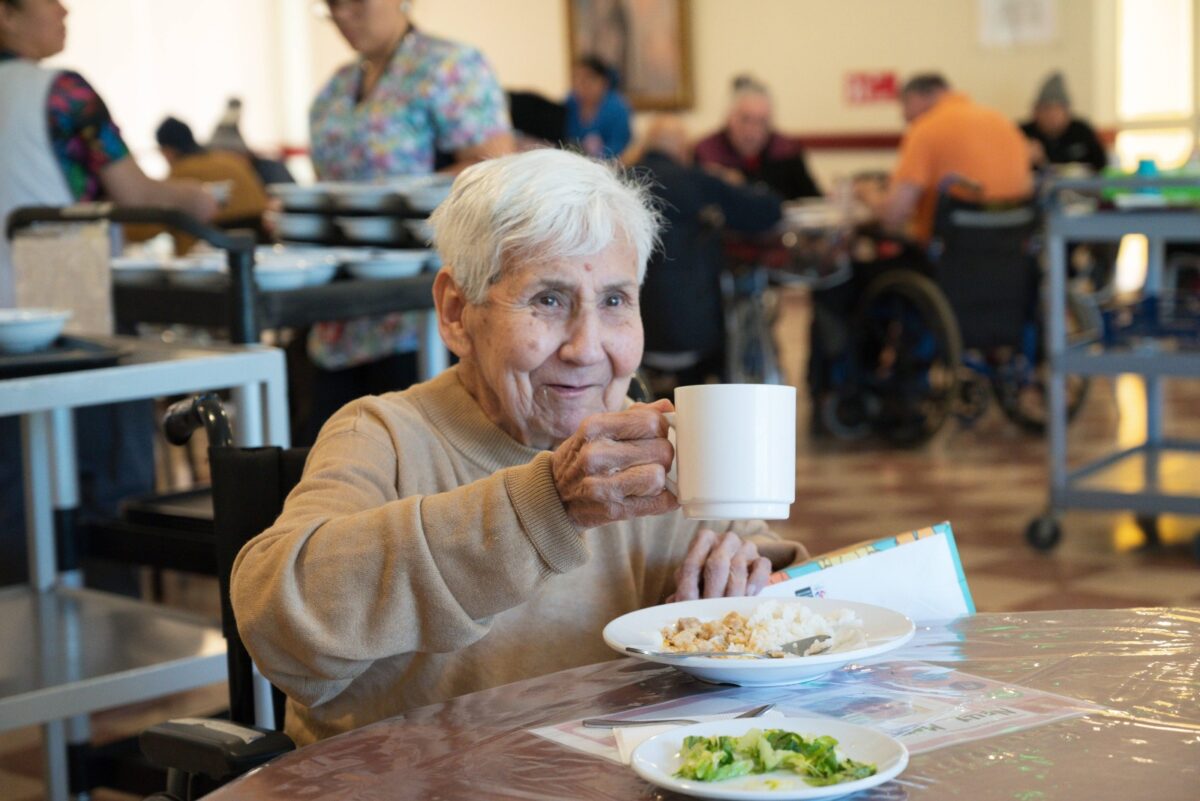 Adulto mayor sonriendo mientras sostiene una taza en el comedor de Fundación Las Rosas.