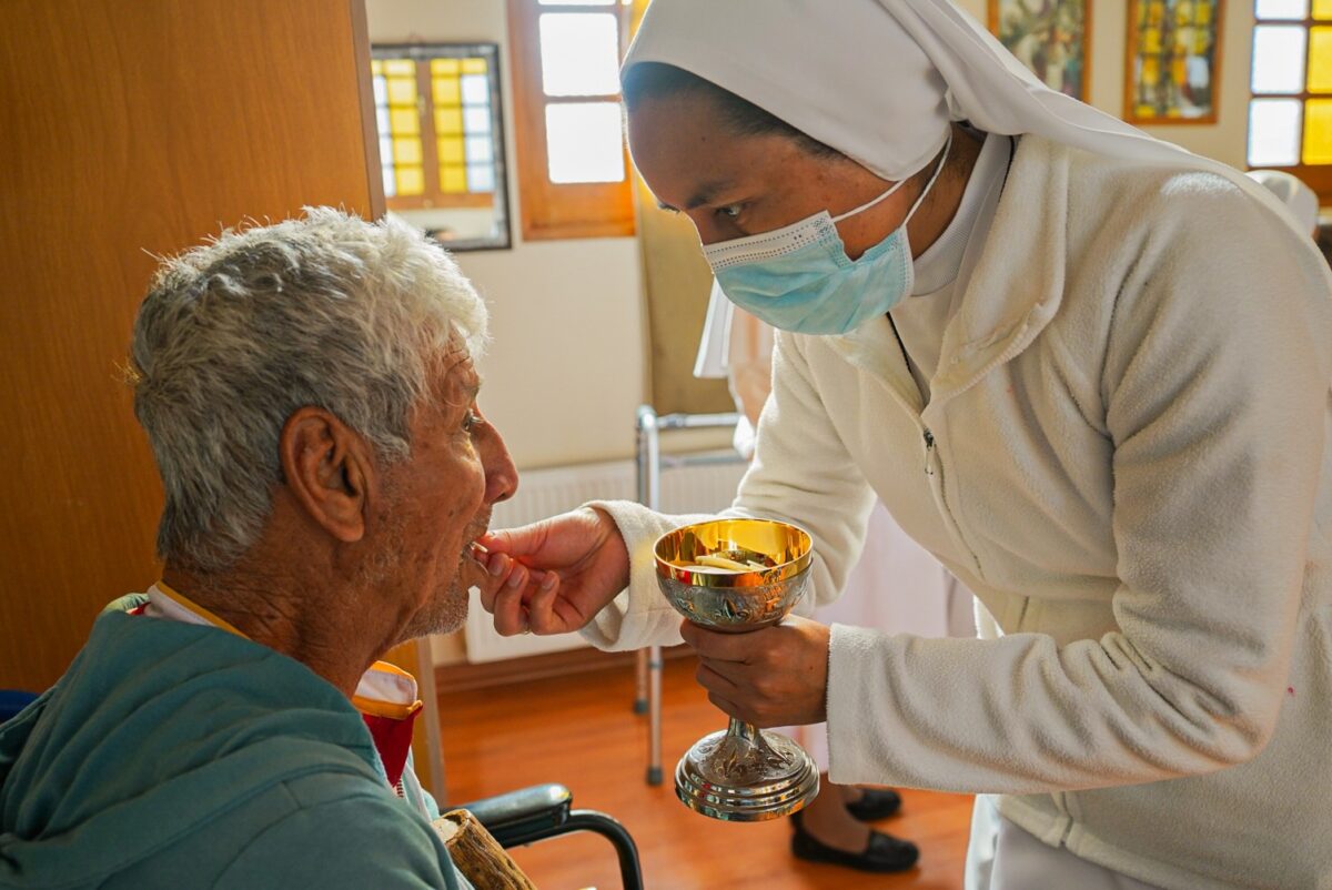 Religiosa con mascarilla entregando la eucaristía a un residente de Fundación Las Rosas.