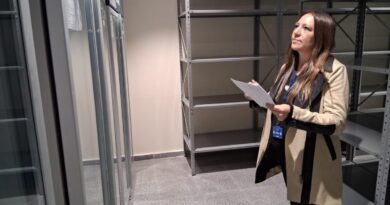 Mujer revisando documentación en una sala con estanterías y equipos.