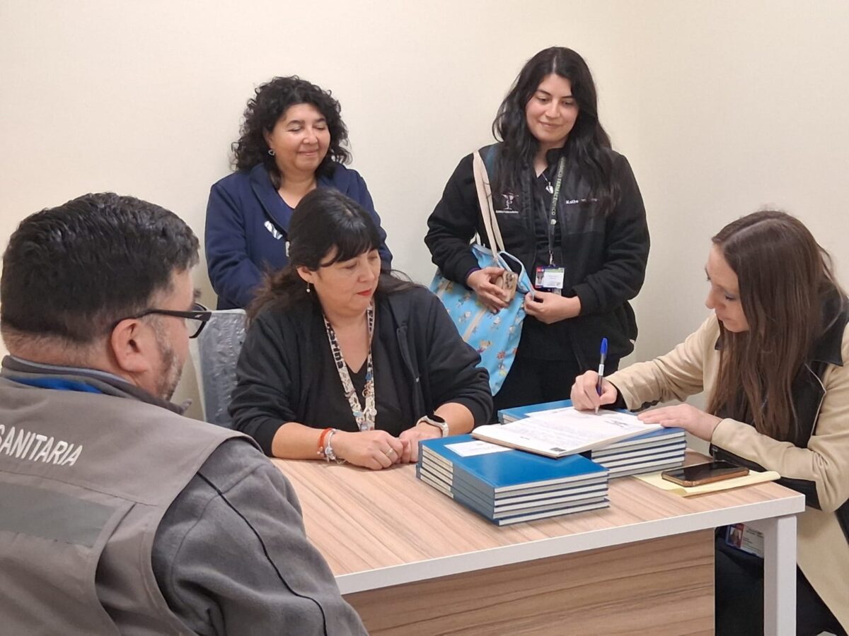 Grupo de personas reunidas alrededor de una mesa, revisando documentos y firmando.