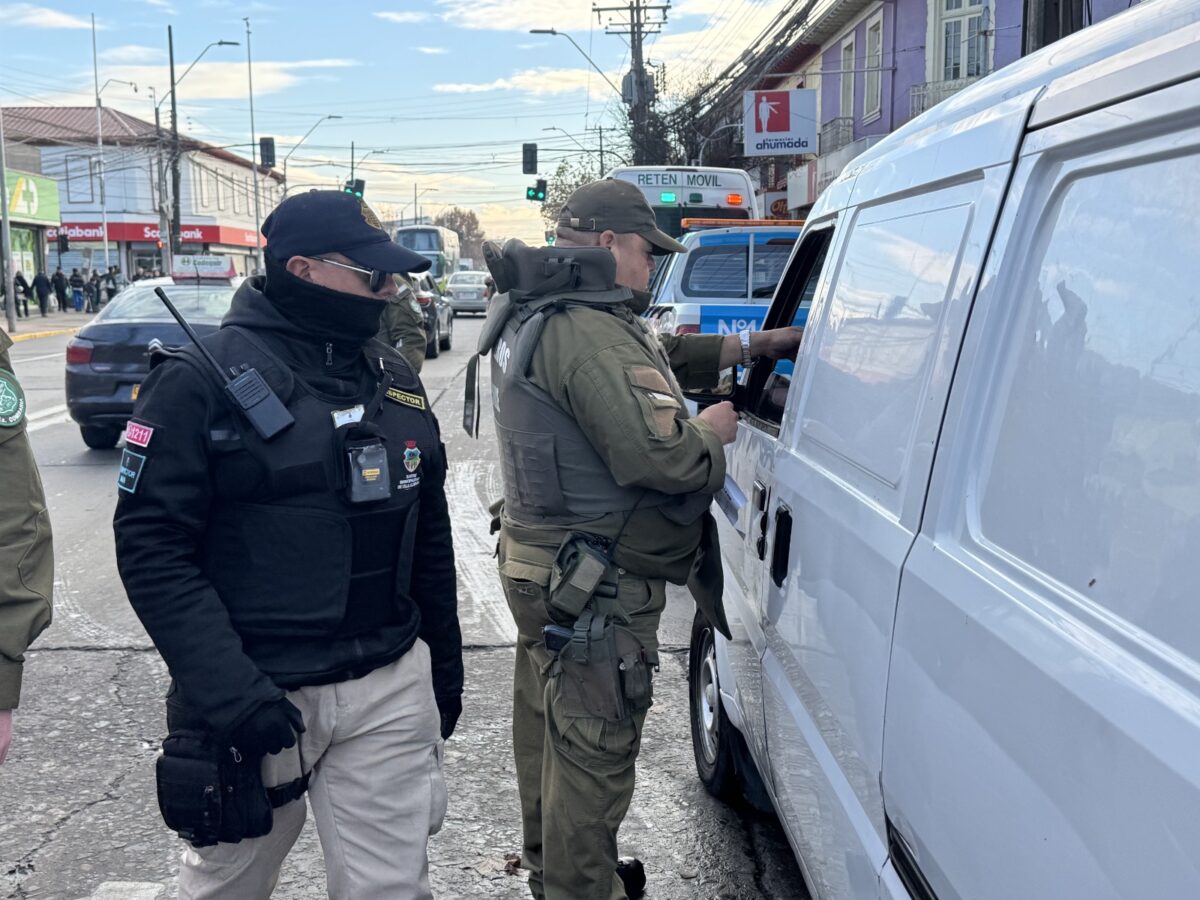 Un oficial de Carabineros observa a otro oficial interactuar con el conductor de una furgoneta blanca.