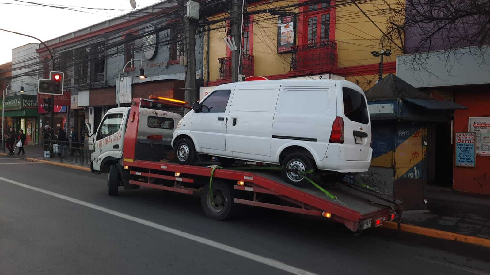 Una furgoneta blanca es transportada en una grúa sobre una calle urbana.