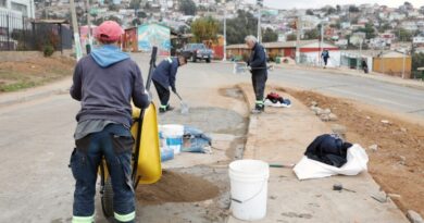 Trabajadores realizan labores de construcción y mejora en un barrio de Valparaíso, con casas asentadas en la ladera de una colina al fondo.